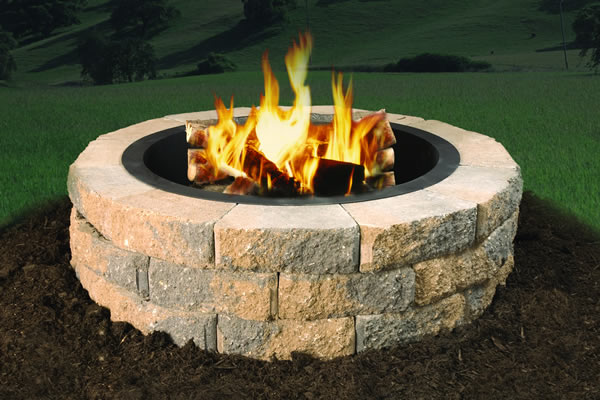 Round stacked-stone fire pit with tall flames set on a mulched lawn