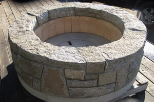 Round custom granite fire pit with a brick-lined interior sitting on a trailer bed.