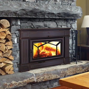 Dark brown wood stove insert set into a gray stacked-stone fireplace beside stacked firewood