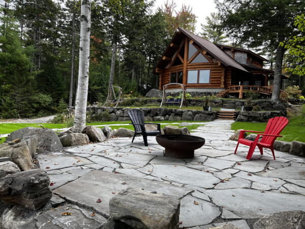 Flagstone patio with blue Adirondack chairs around a fire pit near a log cabin