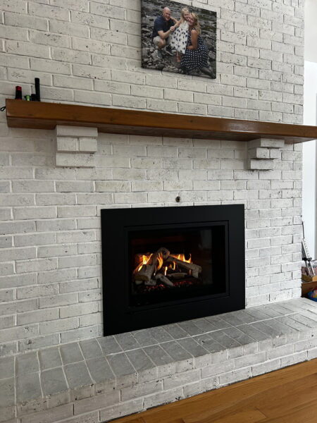 White-painted brick fireplace with a black gas insert and a wood mantel shelf