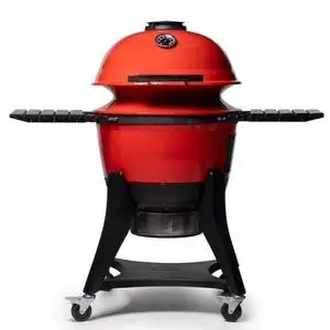 Red ceramic kamado charcoal grill with black side shelves on a rolling stand.