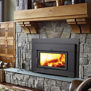 Black wood-burning fireplace insert in a stone hearth with wood mantel and fire tools