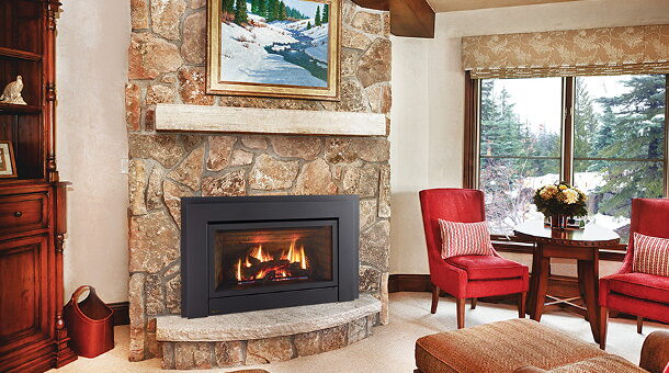 Rounded stone fireplace with a square black gas insert and stone hearth beside red armchairs.
