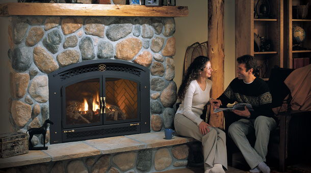 Round river stone fireplace with a black arched gas insert, couple seated on the raised hearth.