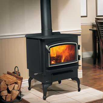 Black freestanding wood stove with nickel trim and a firewood basket on a tile hearth