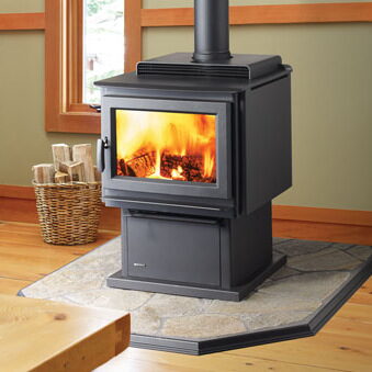 Large black freestanding wood stove with a pedestal base on a stone hearth pad.