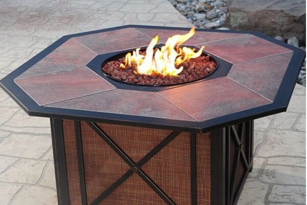 Octagonal slate-top gas fire pit table with a woven wicker base on a patio