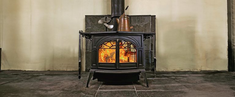 Black cast-iron wood stove with double doors, scrollwork, and a kettle on top