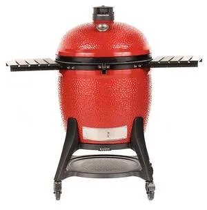 Large red ceramic kamado charcoal grill with side shelves on a rolling black cart.