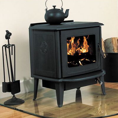 Black cast-iron freestanding wood stove with a kettle on top and a glass hearth pad.