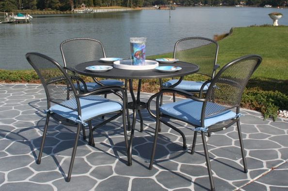 Black wrought iron patio table and chairs with blue cushions beside a waterfront patio