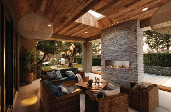 Covered outdoor living space with a stacked-stone linear gas fireplace and wicker sectional