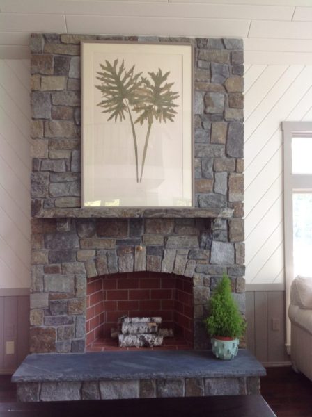 Multicolor stone fireplace with a botanical leaf print above the mantel and birch logs inside