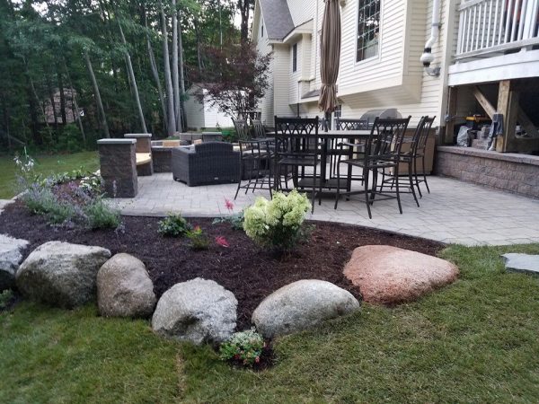 Paver patio with dining table, wicker furniture, and large landscape boulders