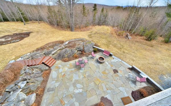Aerial view of a flagstone patio with a fire pit and pink chairs overlooking a mountain meadow.