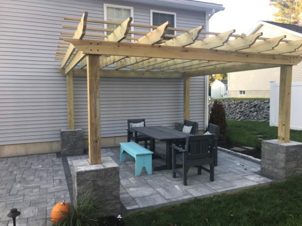 Paver patio under a wood pergola with outdoor dining table, chairs, and a teal bench
