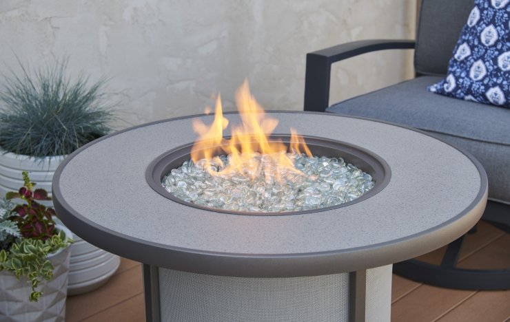 Round gray gas fire pit table with glass flame on a patio