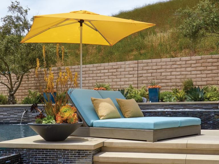 Yellow market umbrella shading a blue chaise lounge beside a pool